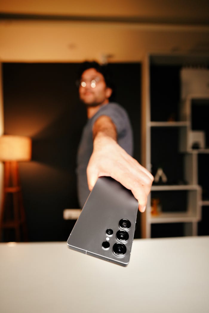 The Art of Drawing Readers In: Your attractive post title goes here A man holds a smartphone towards the camera in a stylish indoor setting, showcasing device features.