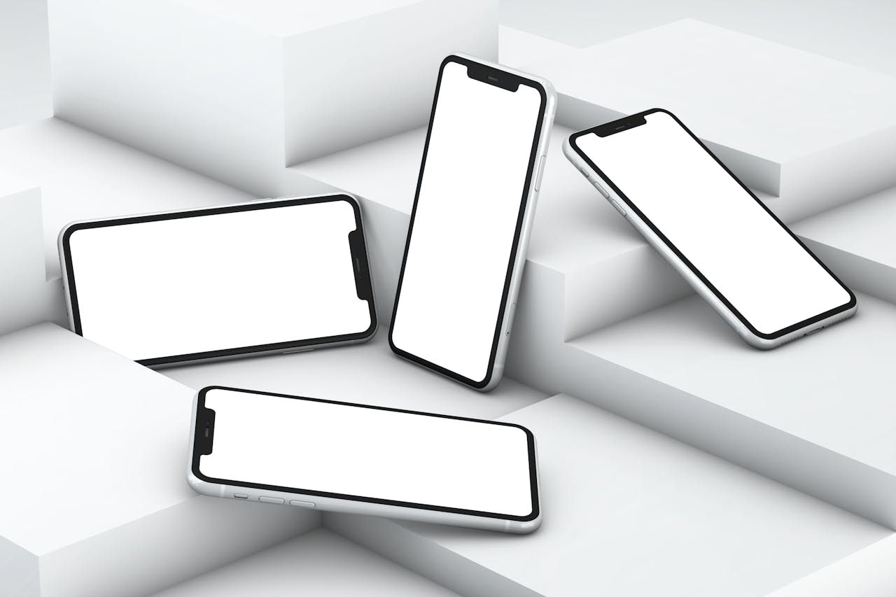 services-01 Four smartphones with white screens arranged on geometric white steps in a minimalist setting.