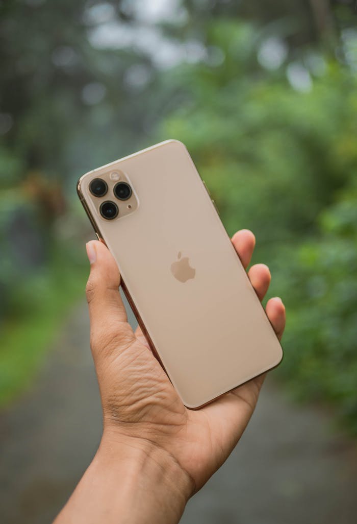 Person holding a modern smartphone outdoors with a blurred natural background.